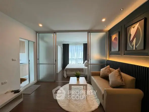 Modern living room with cozy sofa and stylish decor leading to a bright bedroom through sliding glass doors.