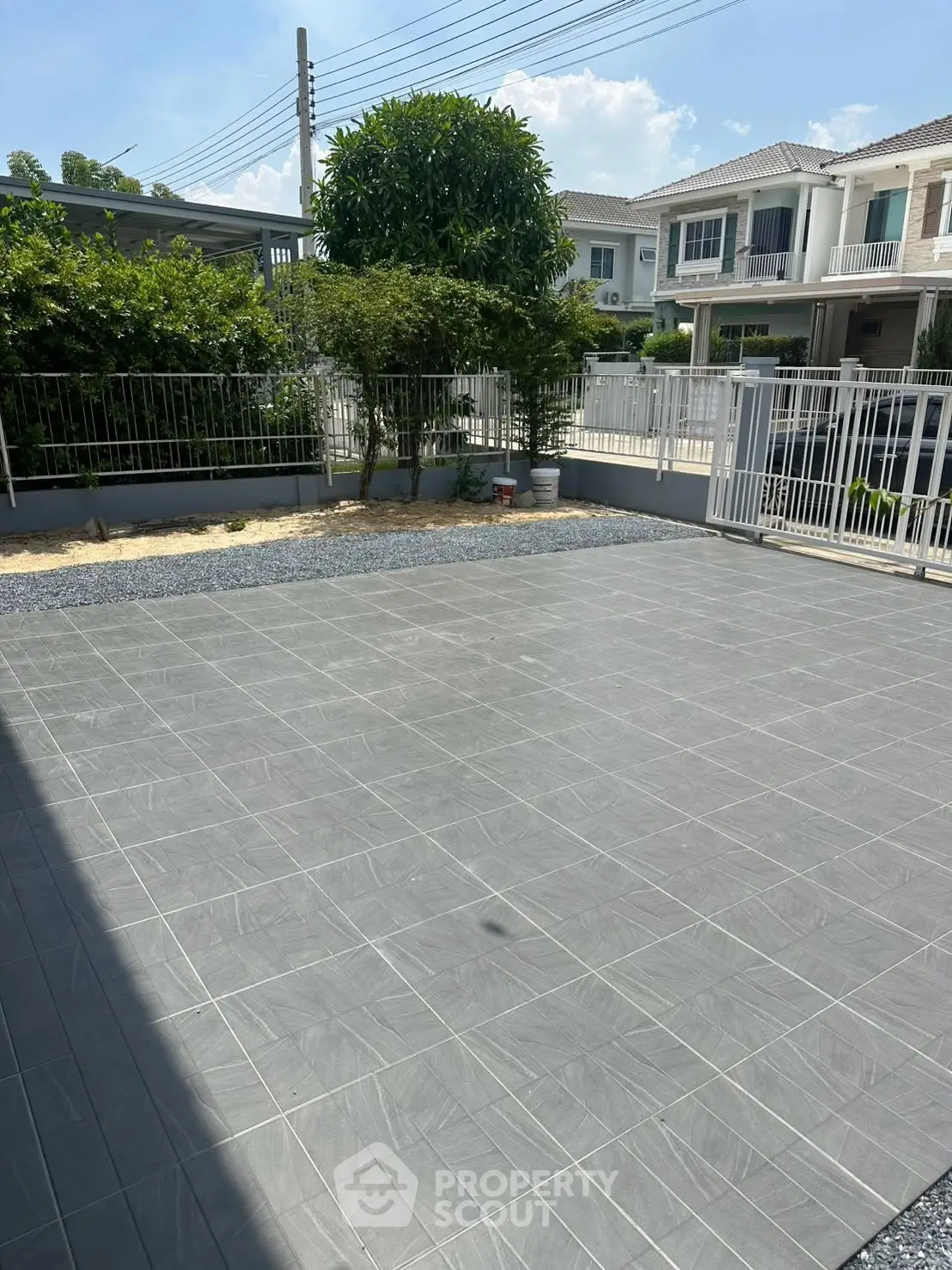 Spacious tiled patio area in modern residential neighborhood with lush greenery.