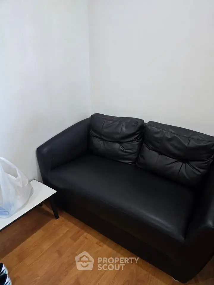 Cozy black leather sofa in a minimalist living room with wooden flooring.