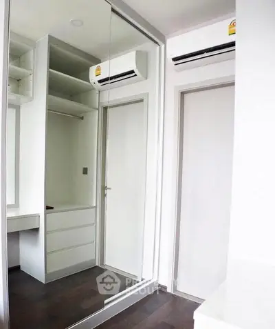 Modern bedroom with mirrored closet and air conditioning unit, featuring sleek design and ample storage space.