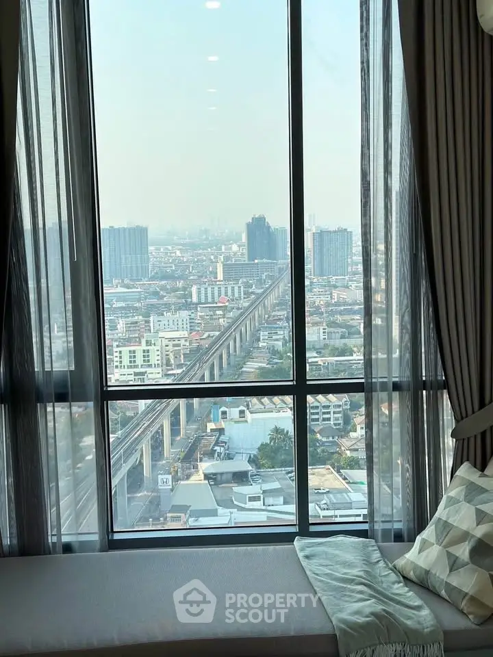 Stunning cityscape view from a high-rise apartment window with cozy seating area.