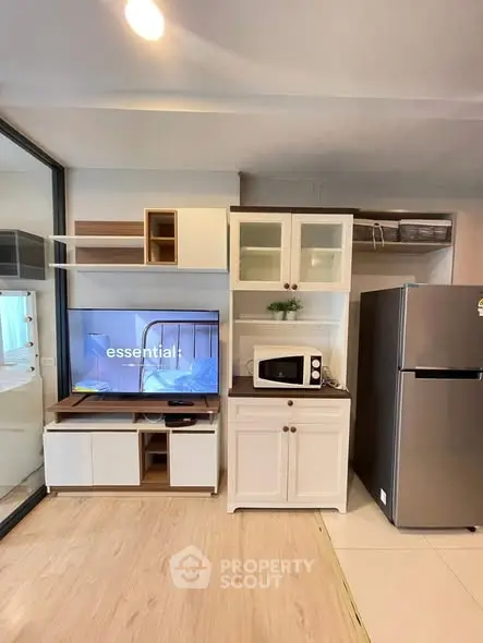 Modern living room with sleek TV unit, microwave, and stainless steel fridge in open layout.