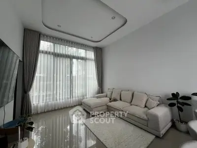 Modern living room with elegant sofa and large window, featuring stylish decor and natural light.