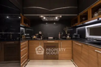 Modern kitchen with sleek wooden cabinets and black countertops, featuring a gas stove and ambient lighting.