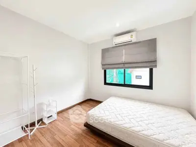 Spacious bedroom with wooden flooring and natural light, featuring a minimalist design and air conditioning.
