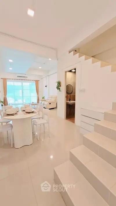 Spacious modern living room with dining area and staircase, featuring elegant decor and natural light.