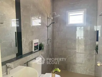 Modern bathroom with sleek tiles and rainfall showerhead, featuring a stylish mirror and natural light.