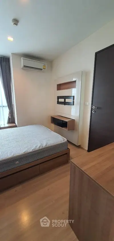 Modern bedroom with wooden flooring, wall-mounted TV space, and air conditioning.