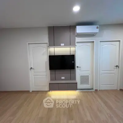 Modern living room with sleek TV setup and wooden flooring, featuring dual doors and air conditioning.