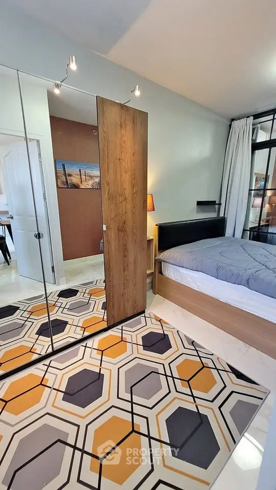 Stylish bedroom with modern decor and geometric rug, featuring mirrored closet and cozy bed setup.