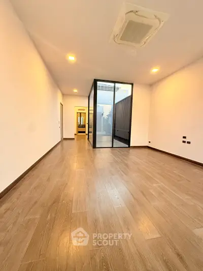 Spacious modern room with wooden flooring and glass partition, ideal for versatile living space.