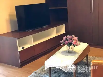 Cozy living room interior with modern entertainment unit, plush carpet, and elegant center table adorned with fresh flowers.