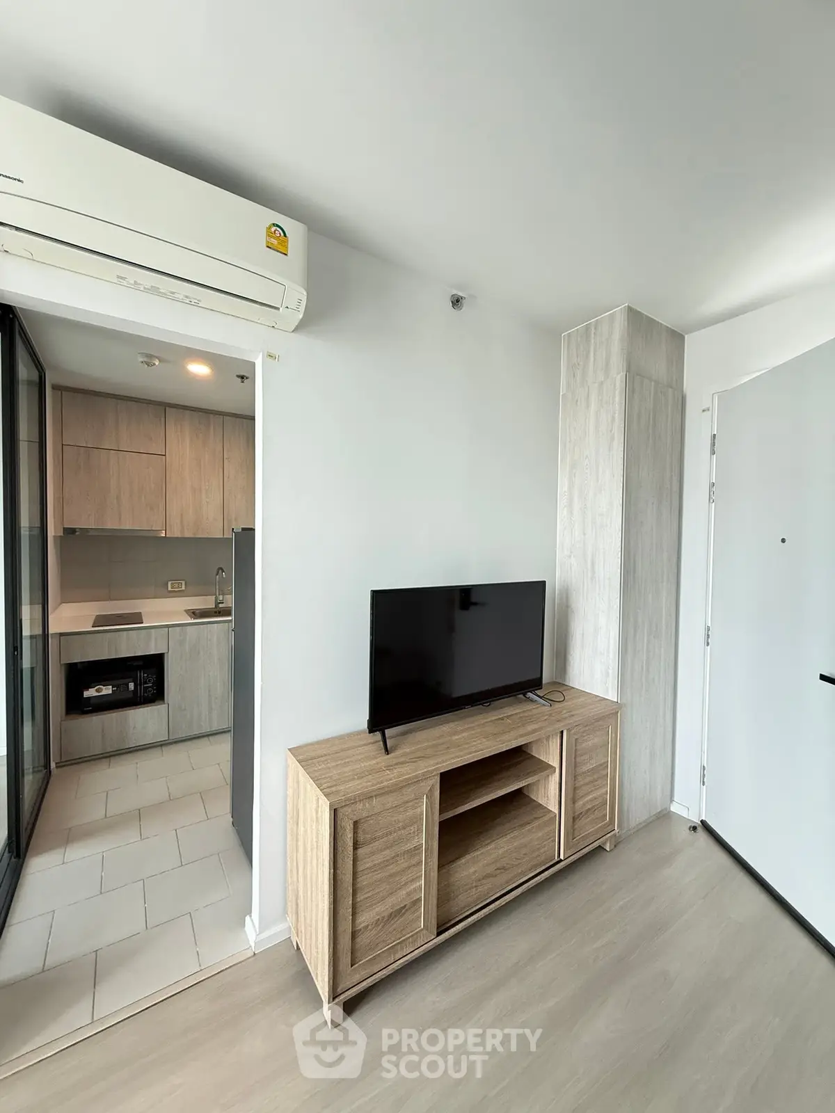 Modern apartment interior with sleek kitchen and cozy living area featuring a TV and air conditioning.