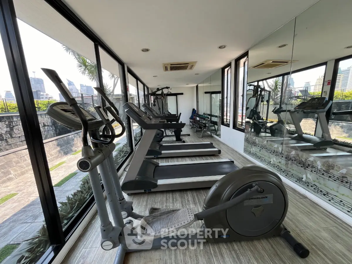 Modern gym with city view, featuring treadmills and exercise bike in a sleek, glass-walled fitness area.