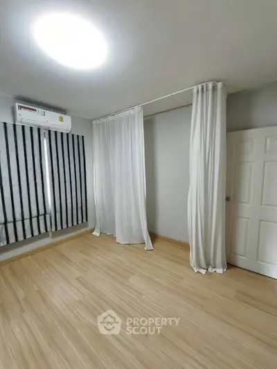 Spacious empty room with wooden flooring and modern air conditioning unit.