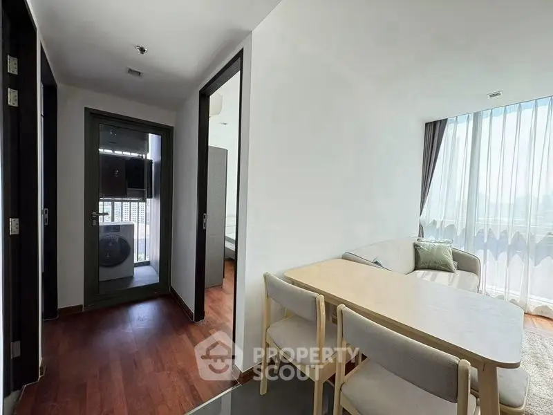 Modern apartment interior with cozy living room and dining area, featuring large windows and wooden flooring.