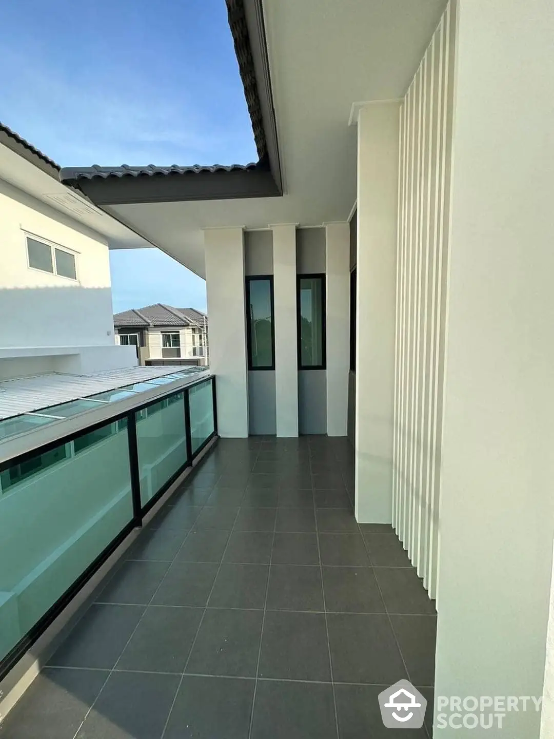 Spacious balcony with modern glass railing, offering a serene outdoor space for relaxation and entertainment, set against a backdrop of neighboring homes under a clear sky.