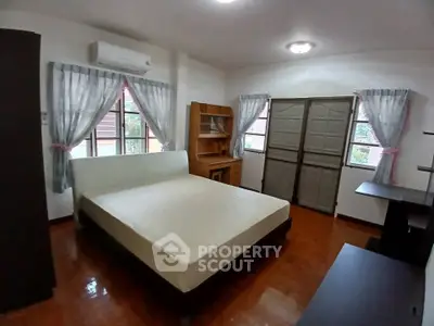 Spacious bedroom with large windows and wooden flooring in a cozy home.