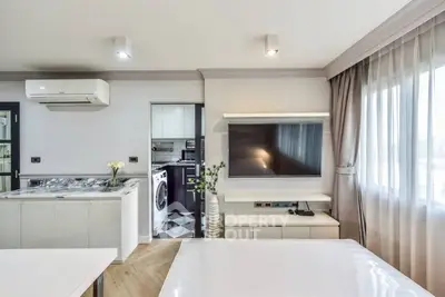 Modern open-plan living room with sleek kitchen and large TV, featuring stylish decor and natural light.