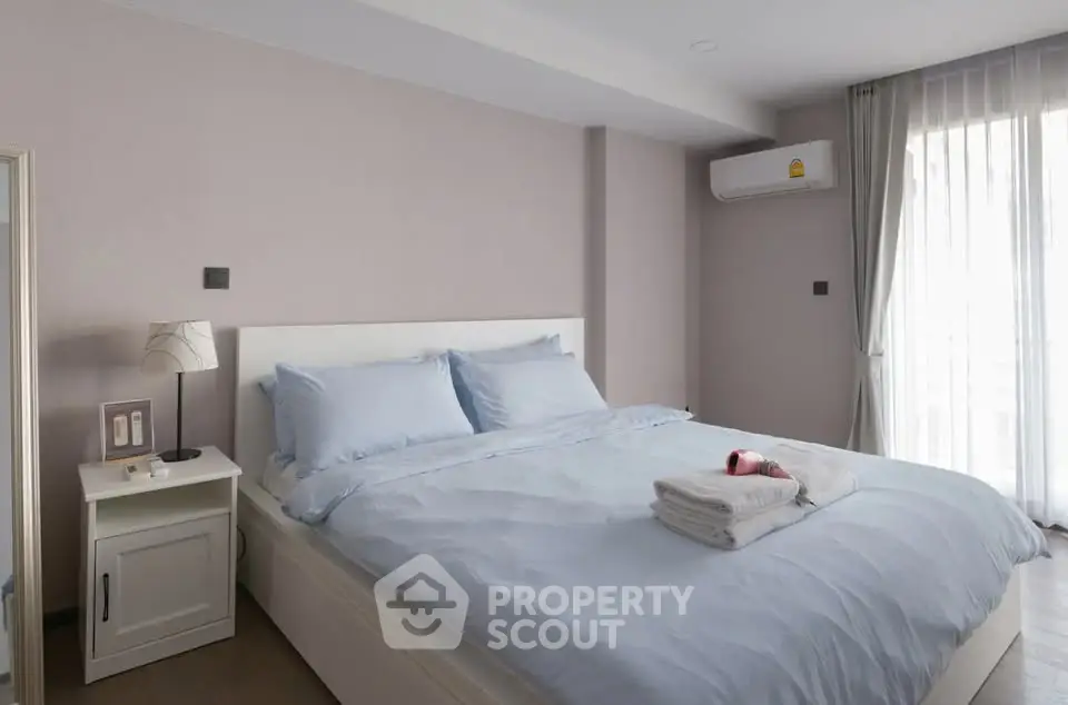 Spacious bedroom with modern decor and natural light, featuring a comfortable bed and air conditioning.