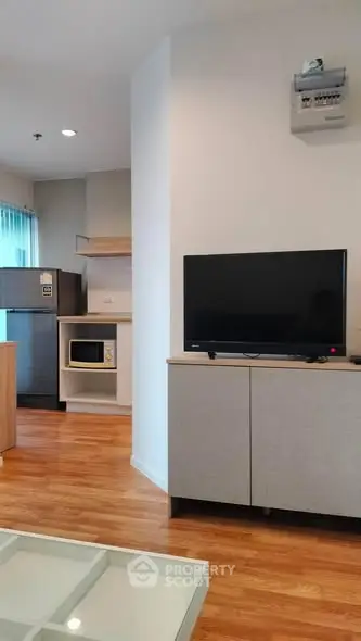 Modern living room with TV, microwave, and fridge in open layout apartment.