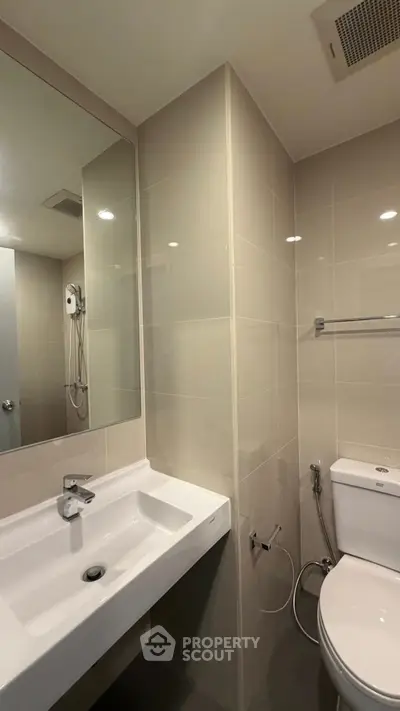 Modern bathroom with sleek fixtures and neutral tiles, featuring a spacious sink and contemporary shower setup.