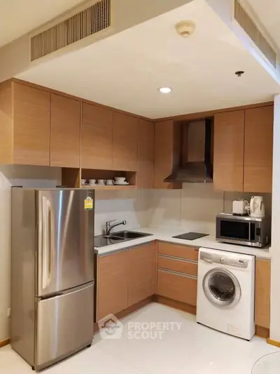 Modern kitchen with wooden cabinets, stainless steel fridge, and washing machine