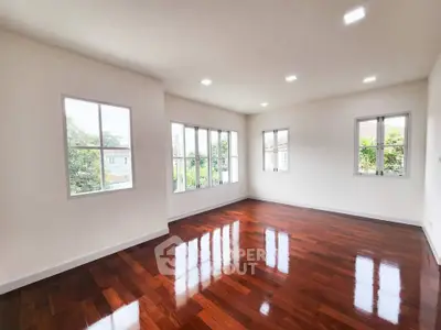 Spacious empty room with polished wooden floors and large windows offering natural light.
