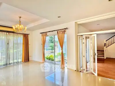 Spacious living room with elegant chandelier and large windows opening to garden view.