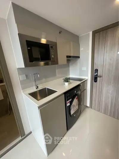 Modern compact kitchen with sleek appliances and stylish cabinetry in a contemporary apartment.