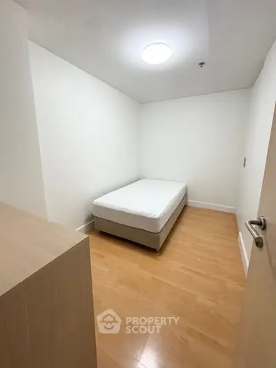 Cozy minimalist bedroom with wooden flooring and a single bed, perfect for a peaceful retreat.