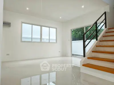Spacious modern living room with sleek staircase and large windows for natural light.