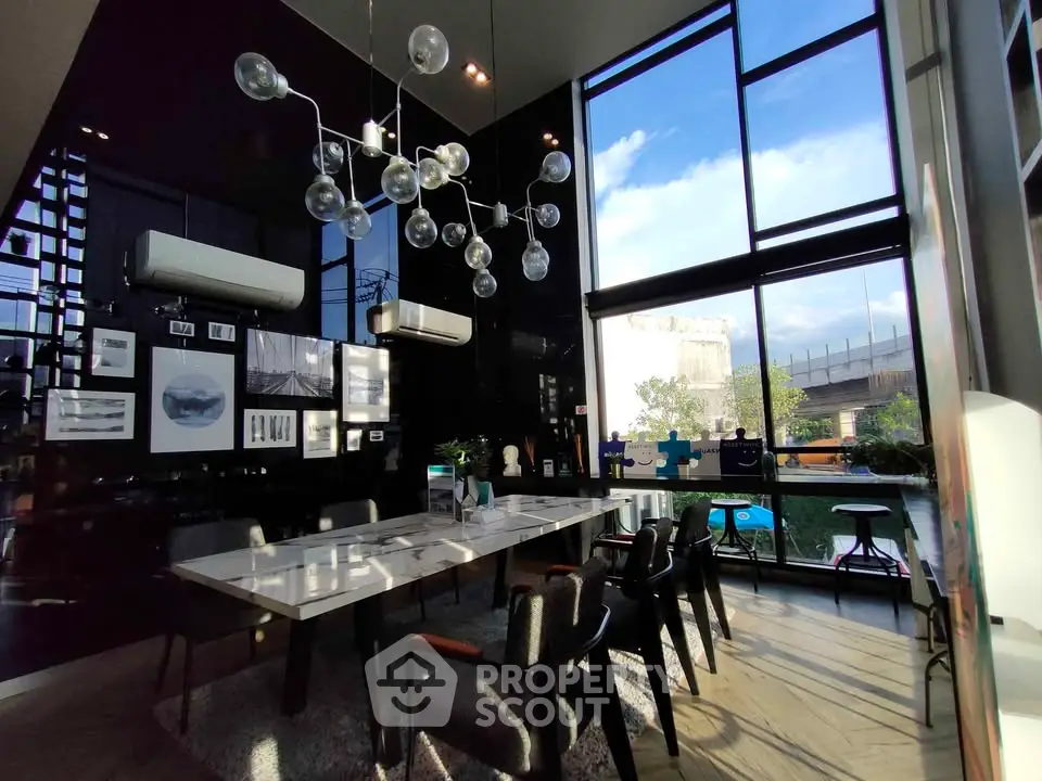 Modern dining area with high ceilings and large windows offering natural light and a stylish chandelier.