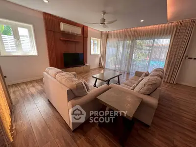 Spacious living room with elegant wooden flooring and large windows overlooking a serene pool view.