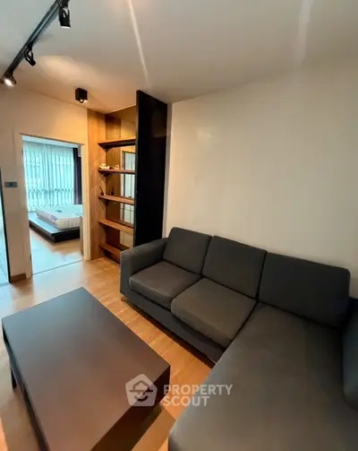 Modern living room with sleek furniture and wooden flooring, leading to a cozy bedroom.