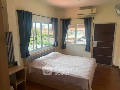 Cozy bedroom with large windows and air conditioning, featuring a comfortable bed and wooden flooring.