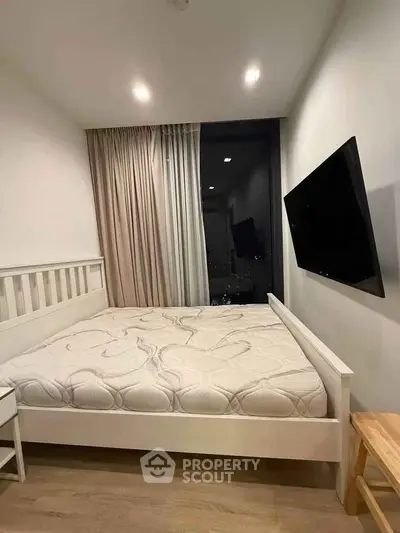 Modern bedroom with large bed and wall-mounted TV, featuring floor-to-ceiling window with city view.