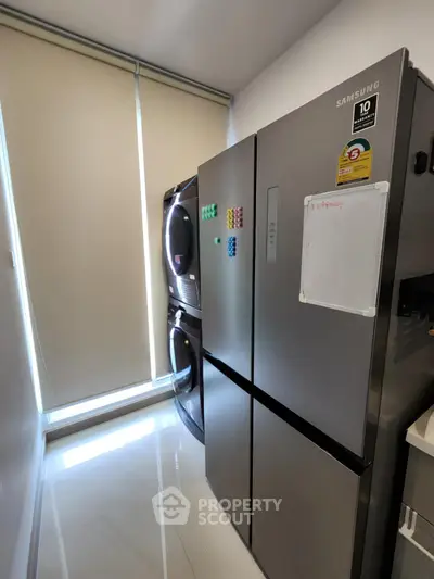 Modern kitchen with sleek Samsung fridge and stacked washer-dryer in bright space.
