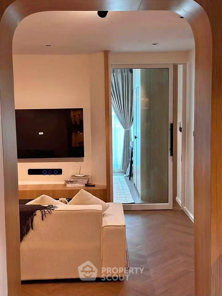 Modern living room with stylish decor and large TV, featuring elegant wooden flooring and cozy seating.