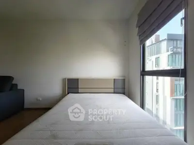 Spacious bedroom with large window and modern bed frame, offering ample natural light.