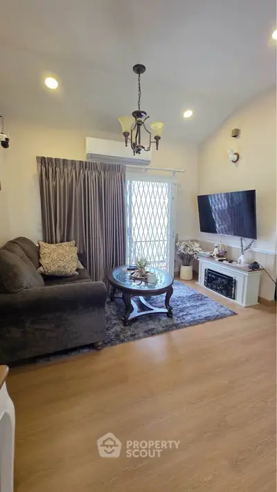 Cozy living room with elegant decor, featuring a plush sofa, stylish chandelier, and wall-mounted TV.
