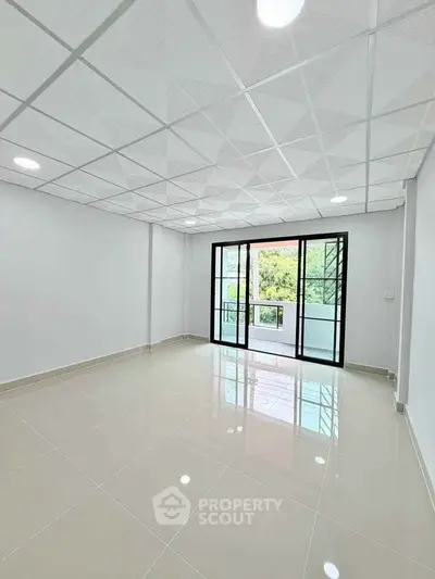 Spacious modern living room with large windows and balcony access, featuring sleek tiled flooring.