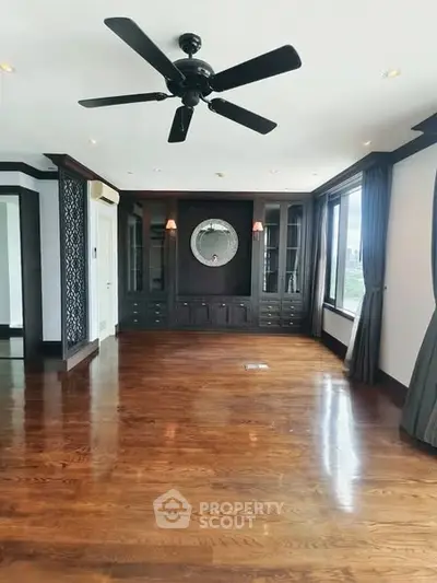 Spacious living room with hardwood floors and ceiling fan, featuring elegant built-in cabinetry.