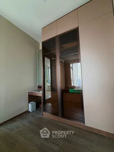 Modern bedroom with sleek wardrobe and wooden flooring, featuring a stylish desk and ample natural light.