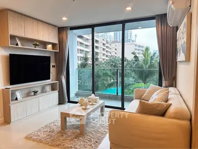 Modern living room with large windows and balcony overlooking lush greenery and pool.