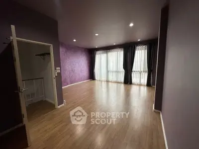 Spacious empty room with wooden flooring and large windows, perfect for customization.