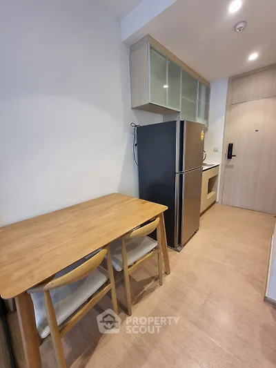 Modern kitchen with sleek fridge and wooden dining set in compact apartment