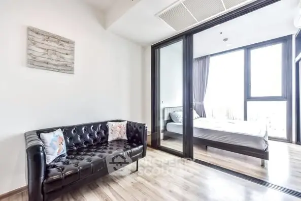 Modern apartment with sleek black sofa and bright bedroom view.