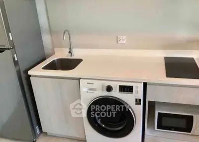 Modern kitchen with washing machine, sink, and microwave in sleek design.