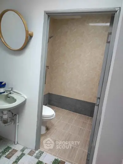 Compact bathroom with shower and round mirror, ideal for small spaces.